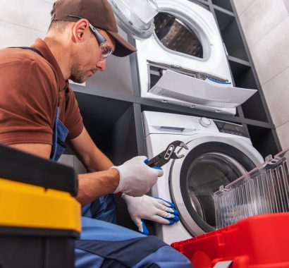 A technician is working on repairing a washing machine in a stylish laundry room, focused on fixing the unit with various tools near him.